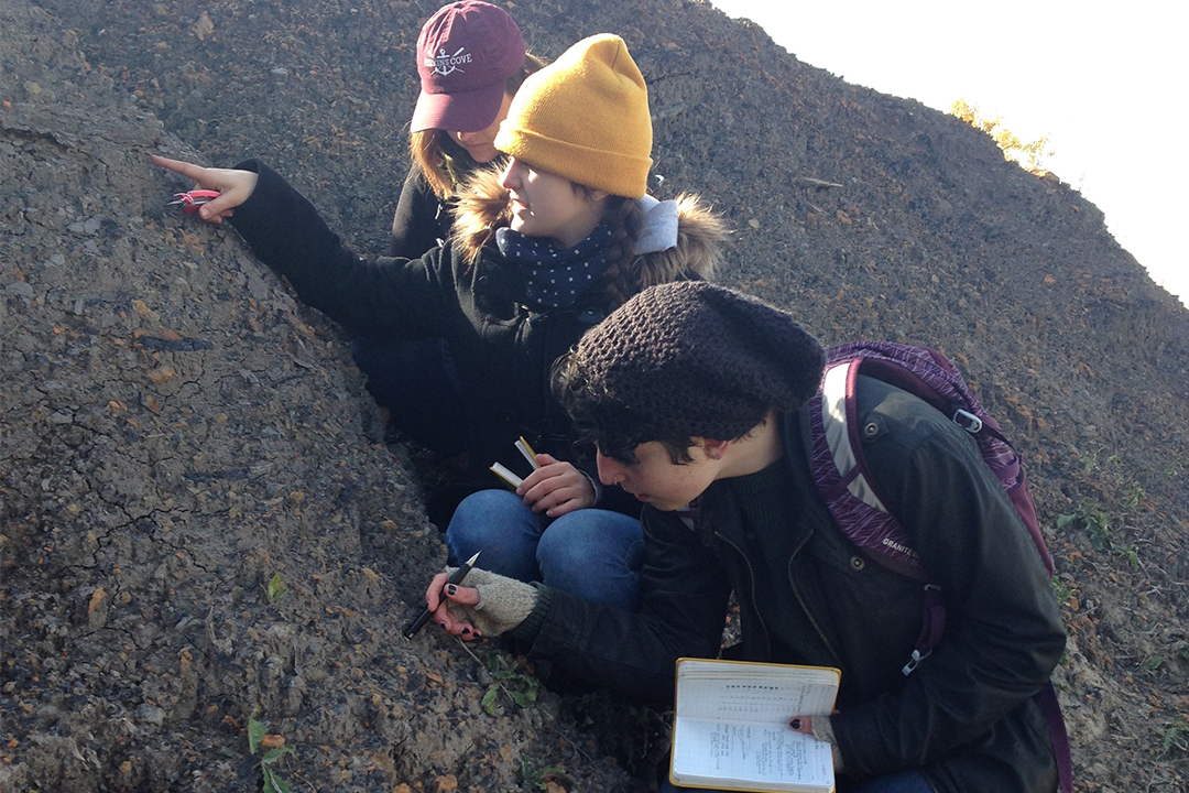 3 students examine a sample of rocks in the field